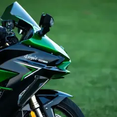 Błyszczący, czarno-zielony motocykl Kawasaki H2 SX z napisem "Ninja H2 SX" na owiewce, zaparkowany na tle zielonej trawy.