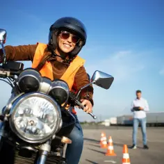 Uśmiechnięta kursantka na motorze, w kasku i kamizelce, uczy się jeździć. Zastanawiasz się, ile kosztuje prawo jazdy na motor?
