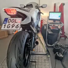 Biały motocykl na hamowni, przygotowany do pomiaru mocy. Widoczna tablica rejestracyjna DOL 1G96. Blokowanie motocykla na A2 to kluczowy etap testów.