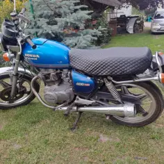 Niebieski motocykl Honda CB250T z pikowanym siedzeniem stoi na trawie.