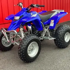 Niebieski Yamaha Blaster 250, gotowy na przygodę na błotnistym torze.
