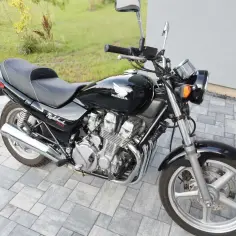 Czarny motocykl Honda CB750 Nighthawk z chromowanymi elementami, zaparkowany na kostce brukowej.