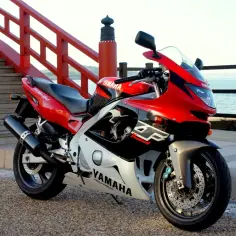 Czerwony motocykl Yamaha Thundercat 600 z czarnymi i białymi akcentami, zaparkowany przy czerwonych schodach i balustradzie nad morzem.