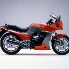 Pomarańczowy motocykl Kawasaki GPZ900R z lat 80. z szarymi wstawkami i czarnym siedzeniem, prezentowany na jasnym tle.
