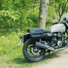 Klasyczny motocykl Honda GB350 z sakwami, zaparkowany na poboczu drogi wśród zieleni i kwitnących krzewów.