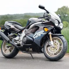 Czarny motocykl Honda CBR 750 Fireblade z lat 90. stoi na drodze, otoczony zielenią.
