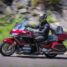 Czerwony motocykl do turystyki we dwoje mknie po drodze, za kierownicą mężczyzna w kasku.