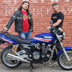 Dwóch mężczyzn stoi obok niebieskiego motocykla Yamaha XJR 1200 na tle ceglanej ściany.