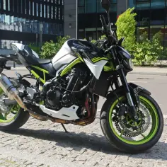 Kawasaki Z900 w miejskiej scenerii, z zielonymi felgami i sportowym wydechem Akrapovič.