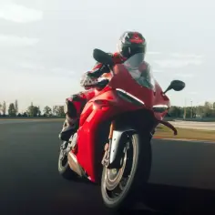 Czerwony motocykl Ducati Panigale V4 S pędzi po torze wyścigowym, kierowca w kombinezonie w tym samym kolorze.