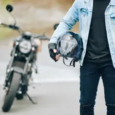 Gotowy na jazdę nowym motocyklem. W ręku trzyma kask, ubrany w jeansową kurtkę i rękawiczki.