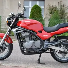Czerwony motocykl Kawasaki ER-5 z czarnym siedzeniem, zaparkowany na chodniku.