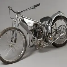 Błyszczący motocykl żużlowy z chromowanymi elementami i grubymi oponami, gotowy do wyścigu na torze.