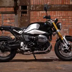 Stylowy motocykl BMW R nineT, jeden z klasycznych naked bikes, z błyszczącym, czarnym bakiem i złotym widelcem, na tle ceglanej ściany.
