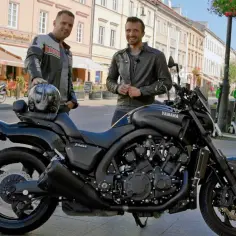 Dwóch mężczyzn pozuje obok czarnego motocykla Yamaha V-Max 1700 na ulicy.