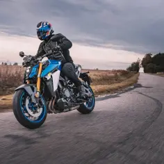 Motocyklista w kasku jedzie sportowym motocyklem po drodze wśród pól.