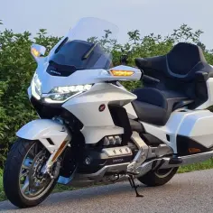 Biały Honda Goldwing 1800, choć luksusowy, ma swoje wady. Widoczny na tle zieleni, z potężnym silnikiem i wygodnym siedzeniem.