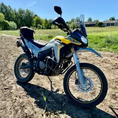 Żółto-szary motocykl typu adventure, gotowy do podboju terenu. Ten **dominar** dróg i bezdroży czeka na przygodę.