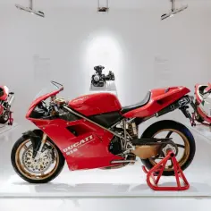 Trzy czerwone motocykle Ducati, w tym model 916, na białym tle ekspozycji muzealnej.