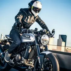 Motocyklista w kasku i skórzanej kurtce pędzi na motocyklu Husqvarna Vitpilen 701 przez miasto.