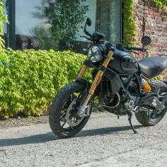 Czarny Ducati Scrambler 1100, gotowy na przygodę, zaparkowany przy ceglanej ścianie porośniętej bluszczem.