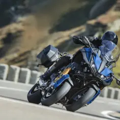 Motocyklista na niebieskim Yamaha Niken pochyla się na zakręcie górskiej drogi, ciesząc się jazdą.