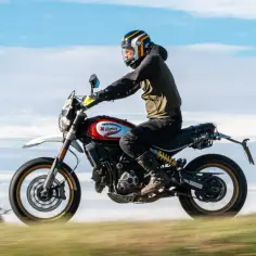 Motocyklista w kasku jedzie na motocyklu Scrambler. Czy to "power bomb 4t co daje" taki efekt?