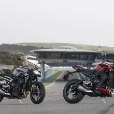 Dwa motocykle Triumph Street Triple, jeden czarny, drugi czerwony, stoją na torze wyścigowym.