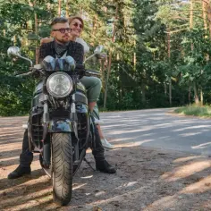 Para motocyklistów na czarnym motocyklu na leśnej drodze.