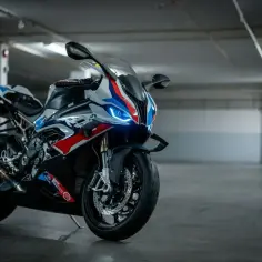 Sportowy motocykl BMW XR w biało-niebiesko-czerwonych barwach, z włączonymi światłami LED, zaparkowany w garażu.