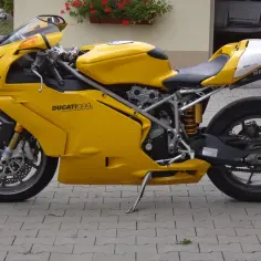 Żółty motocykl Ducati 999s z czarnym siedzeniem i białymi akcentami, zaparkowany na chodniku z kostki brukowej.