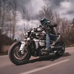 Motocyklista na Triumph Rocket 3, którego dane techniczne budzą podziw, pędzi drogą wśród drzew.
