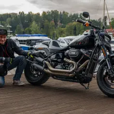 Mężczyzna w czapce Harley-Davidson pozuje obok swojego motocykla Harley Davidson Dyna na drewnianym pomoście.