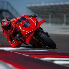 Motocyklista w czerwonym kombinezonie pochyla się na torze wyścigowym na swoim Ducati Panigale V4.