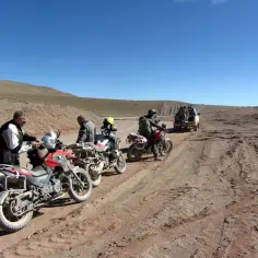Zjazd motocyklowy w pustynnym krajobrazie. Motocykliści w pełnym rynsztunku, motocykle terenowe i samochód terenowy na piaszczystej drodze.