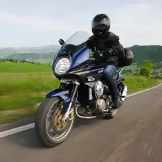 Motocyklista na niebieskim motocyklu szosowo turystycznym przemierza krętą drogę wśród zielonych wzgórz.
