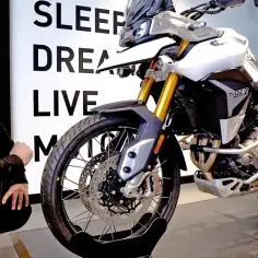 Mężczyzna w czarnej kurtce ogląda biały motocykl Triumph Tiger 900.