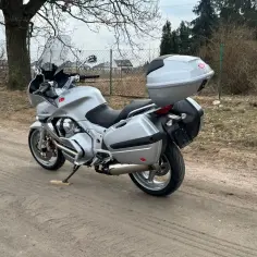 Srebrny motocykl Moto Guzzi Norge z kuframi, gotowy na podróż po wiejskich drogach.