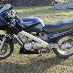 Granatowy motocykl Honda NTV Revere z napędem wałowym, zaparkowany na trawie.