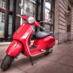 Czerwona karta motorowerowa Vespa stoi na chodniku przed budynkiem.