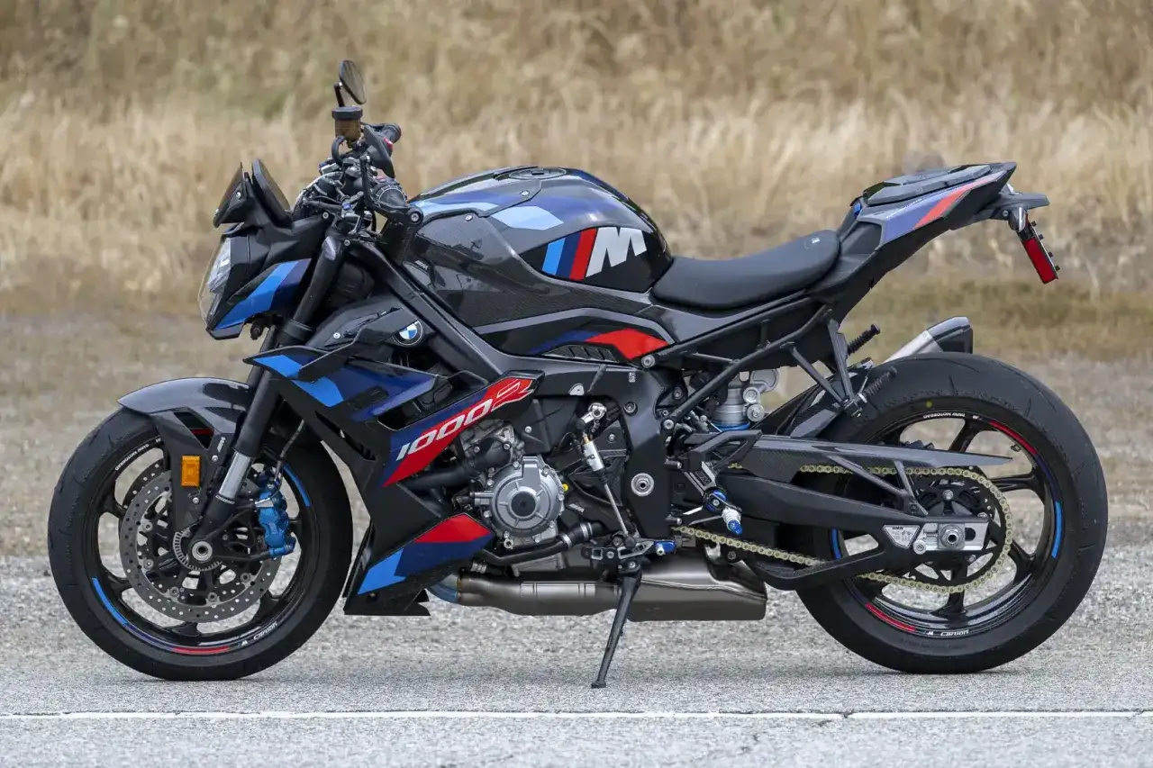 Czarny motocykl BMW M 1000 R z niebieskimi i czerwonymi akcentami, stojący na drodze.