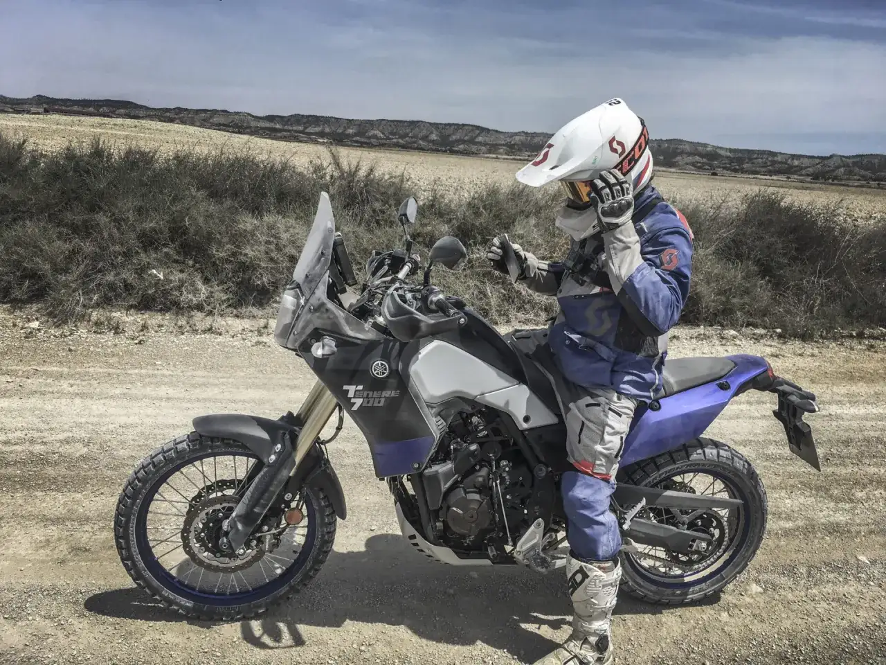 Motocyklista w kasku i stroju terenowym siedzi na motocyklu Yamaha Tenere 700. Wysokość siedzenia pozwala na pewne oparcie stóp na ziemi.
