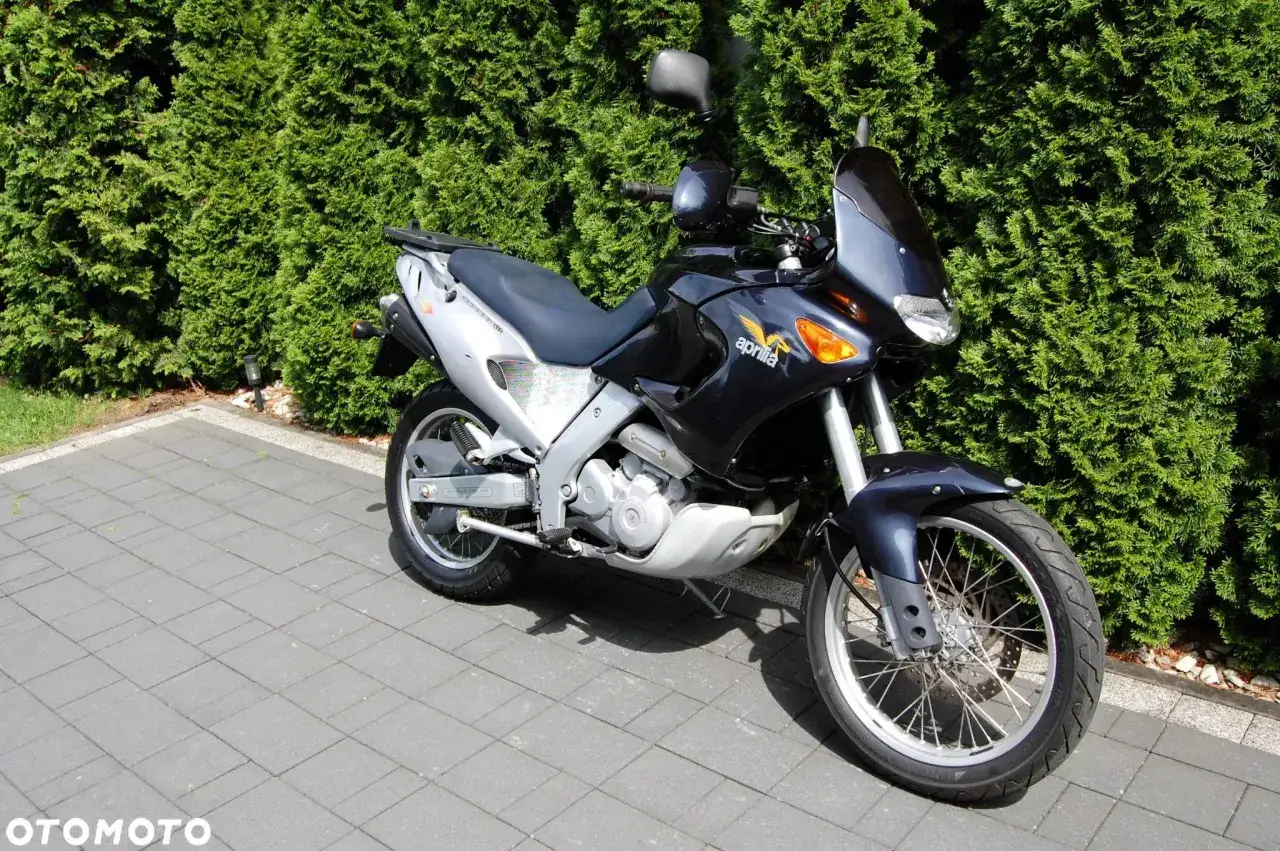 Ciemnoniebieski motocykl Aprilia Pegaso stoi na wybrukowanym podjeździe przed żywopłotem.