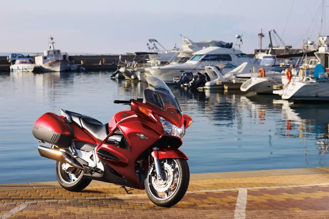 Czerwony motocykl Honda ST 1300 w marinie. Choć jego wady są dyskusyjne, wygląda imponująco na tle jachtów.