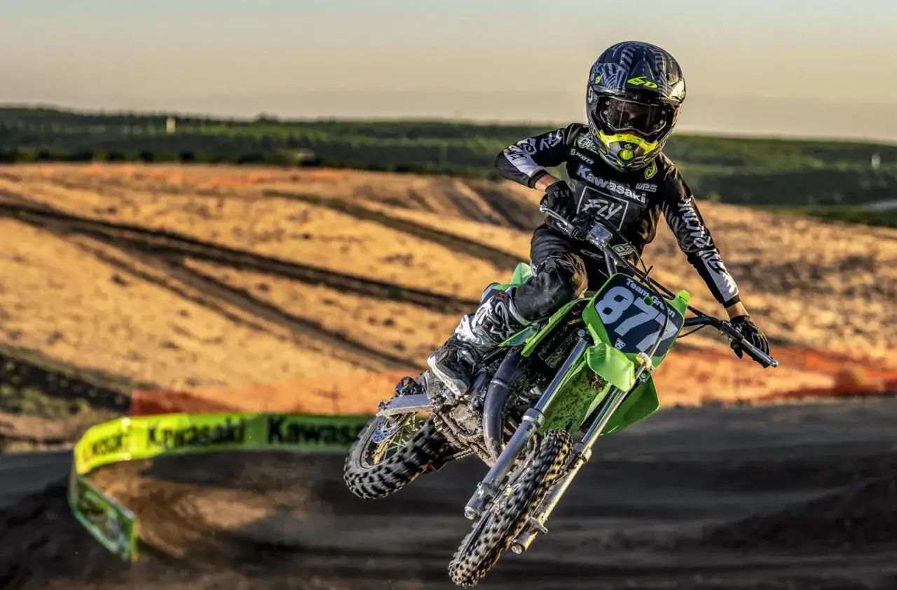 Młody motocyklista na zielonym Kawasaki KX 65 w powietrzu. Ile ma koni? To pytanie zadaje sobie wielu fanów tego zwinnego crossa.