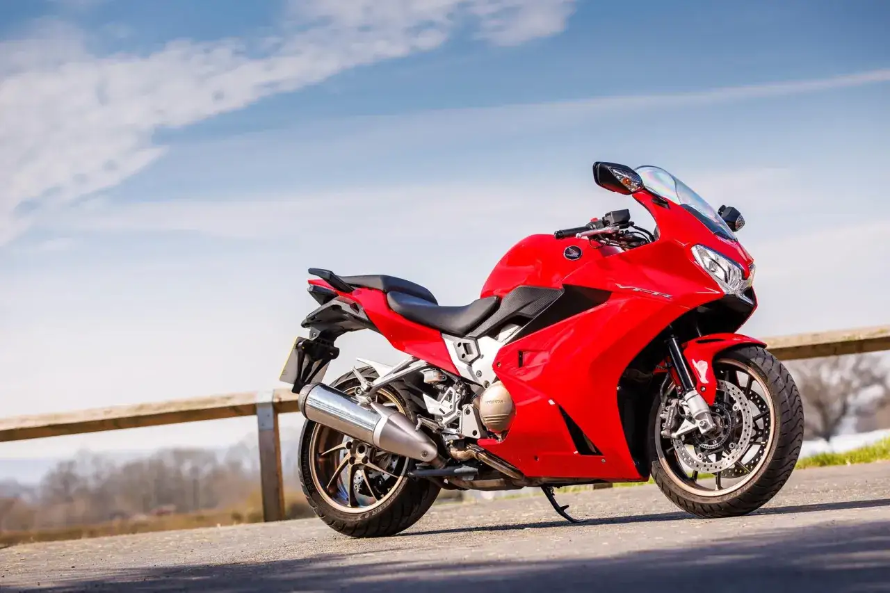 Czerwony motocykl Honda VFR 800 VTEC zaparkowany na tle błękitnego nieba z chmurami.