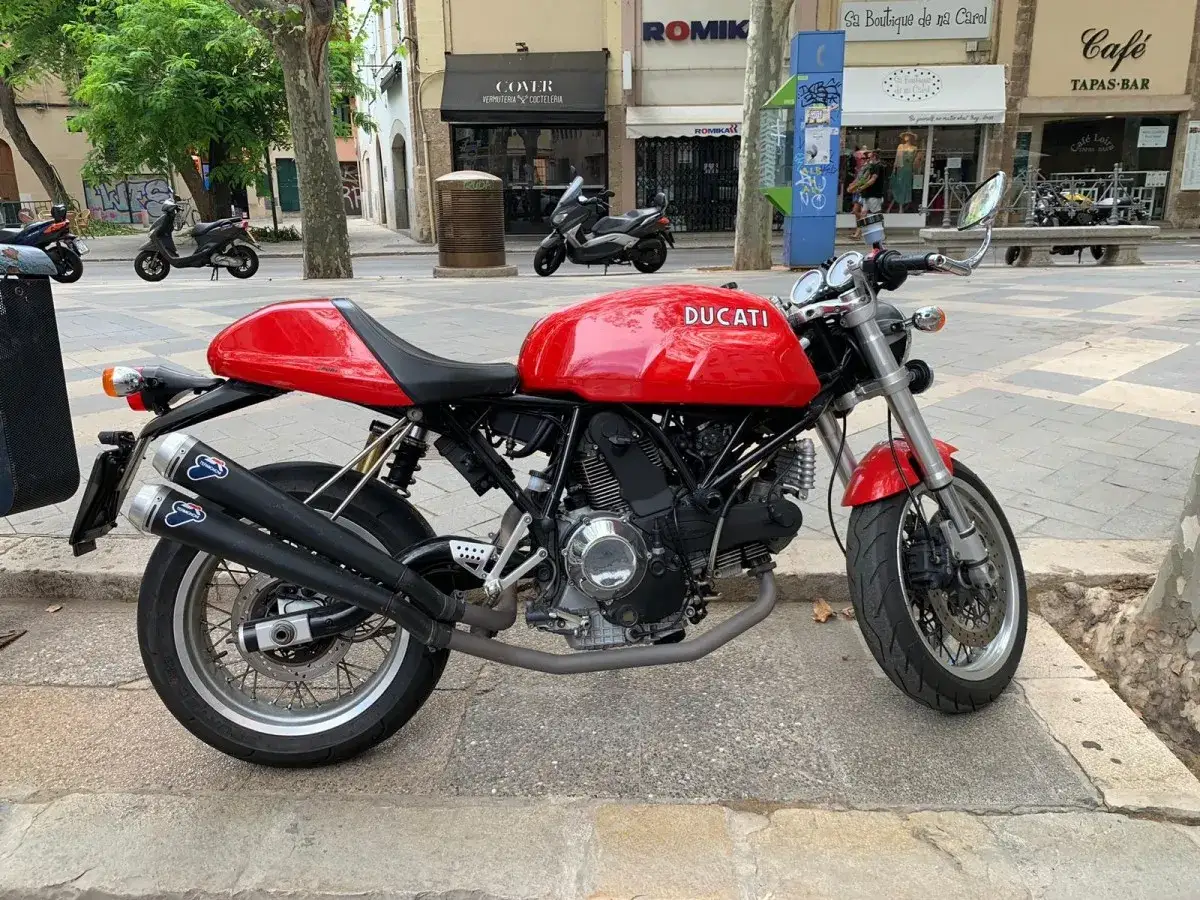 Czerwony Ducati Monster 600 z podwójnym wydechem Termignoni, zaparkowany na chodniku w mieście.
