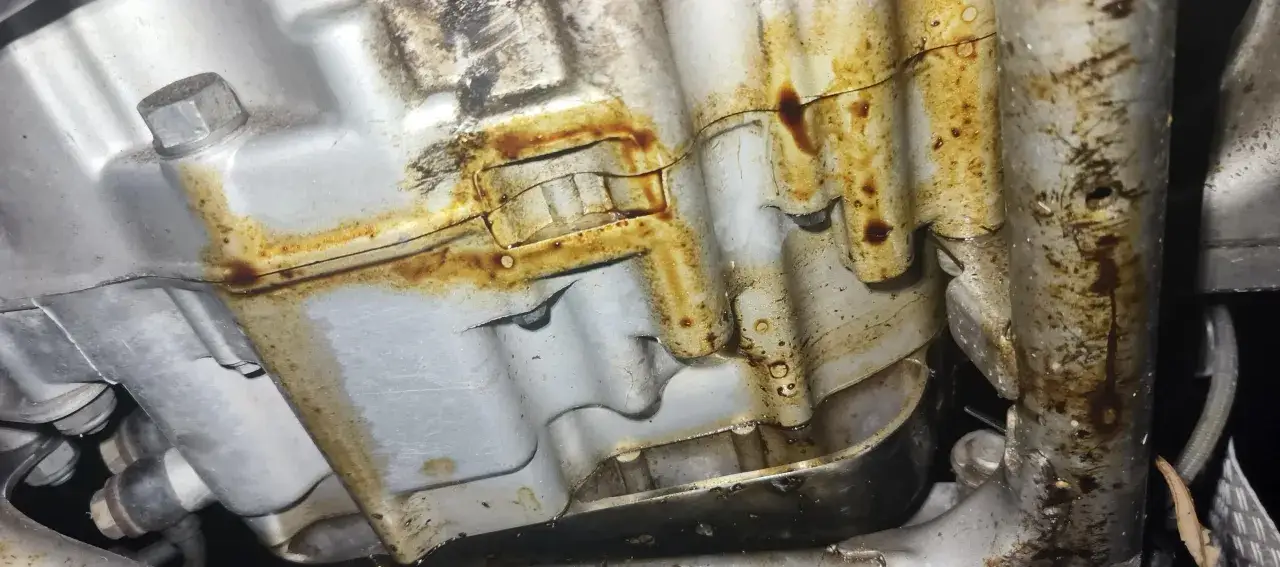 Widoczny wyciek oleju z silnika motocyklowego. Brązowe ślady i krople oleju na metalowych elementach sugerują problem.