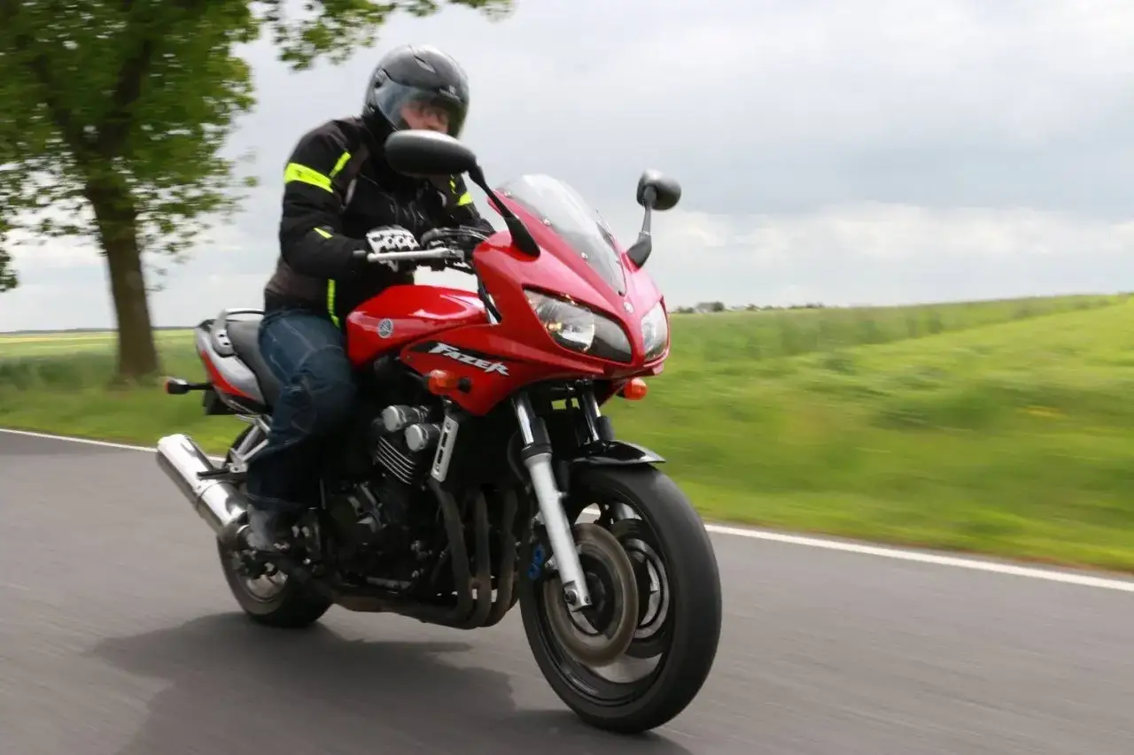 Czerwony motocykl Yamaha Fazer 600 w ruchu, kierowca w kasku i kurtce, na tle zielonych pól. Dane techniczne tego modelu są imponujące.
