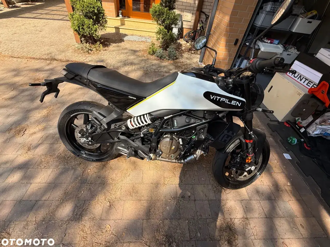 Stojący na bruku motocykl Husqvarna Vitpilen 701 w białym malowaniu z żółtym akcentem.